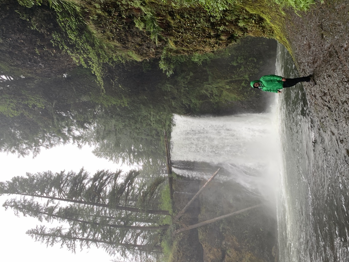Ian Michael Flores standing at the foot of a waterfall in a green gorge