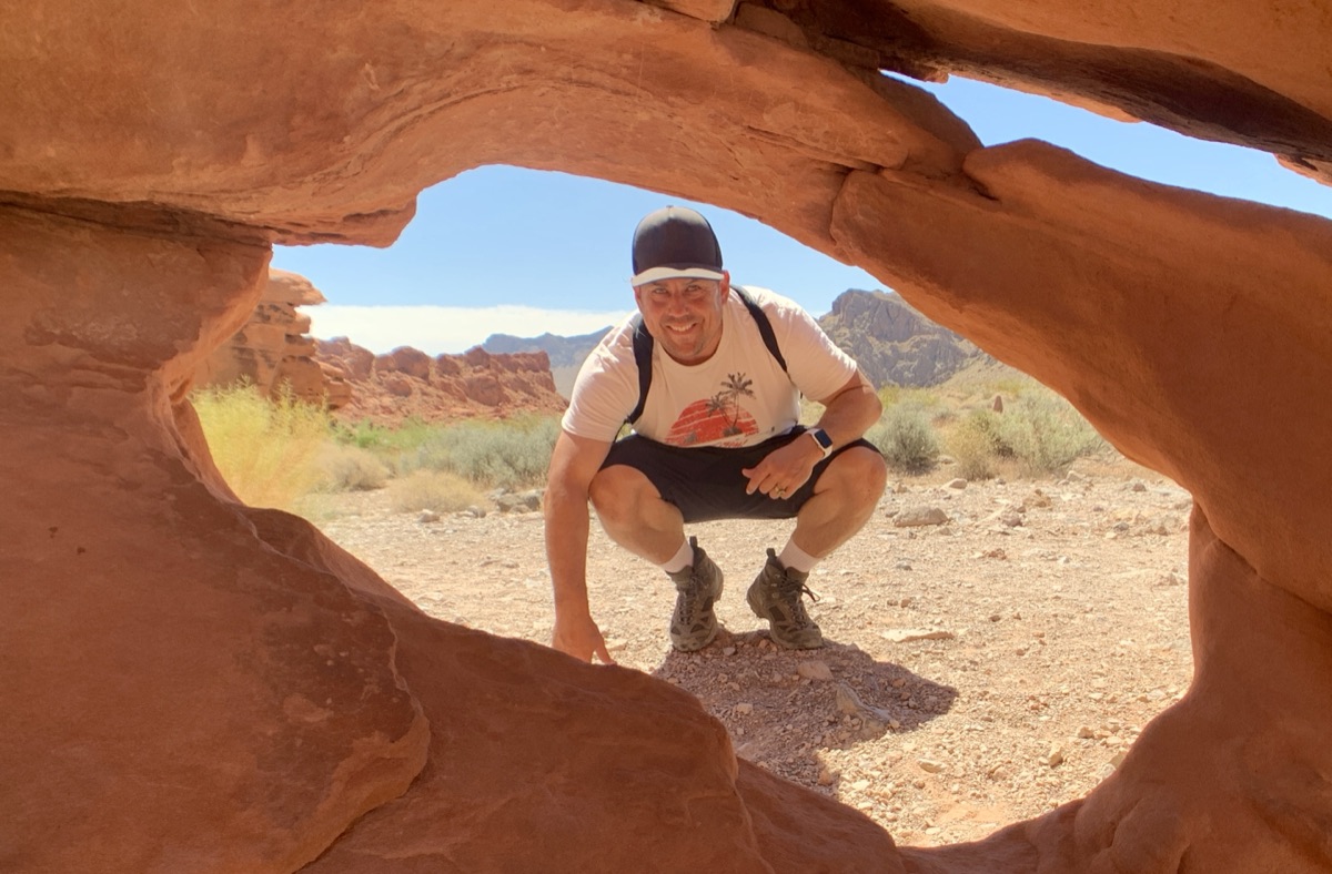 Ian Michael Flores framed by a sandstone arch in the Valley of Fire, the desert opening out behind him