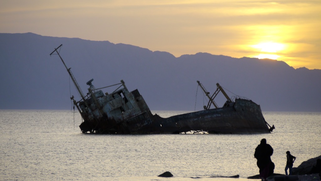 Two figures on the rocks, the wreck beyond them